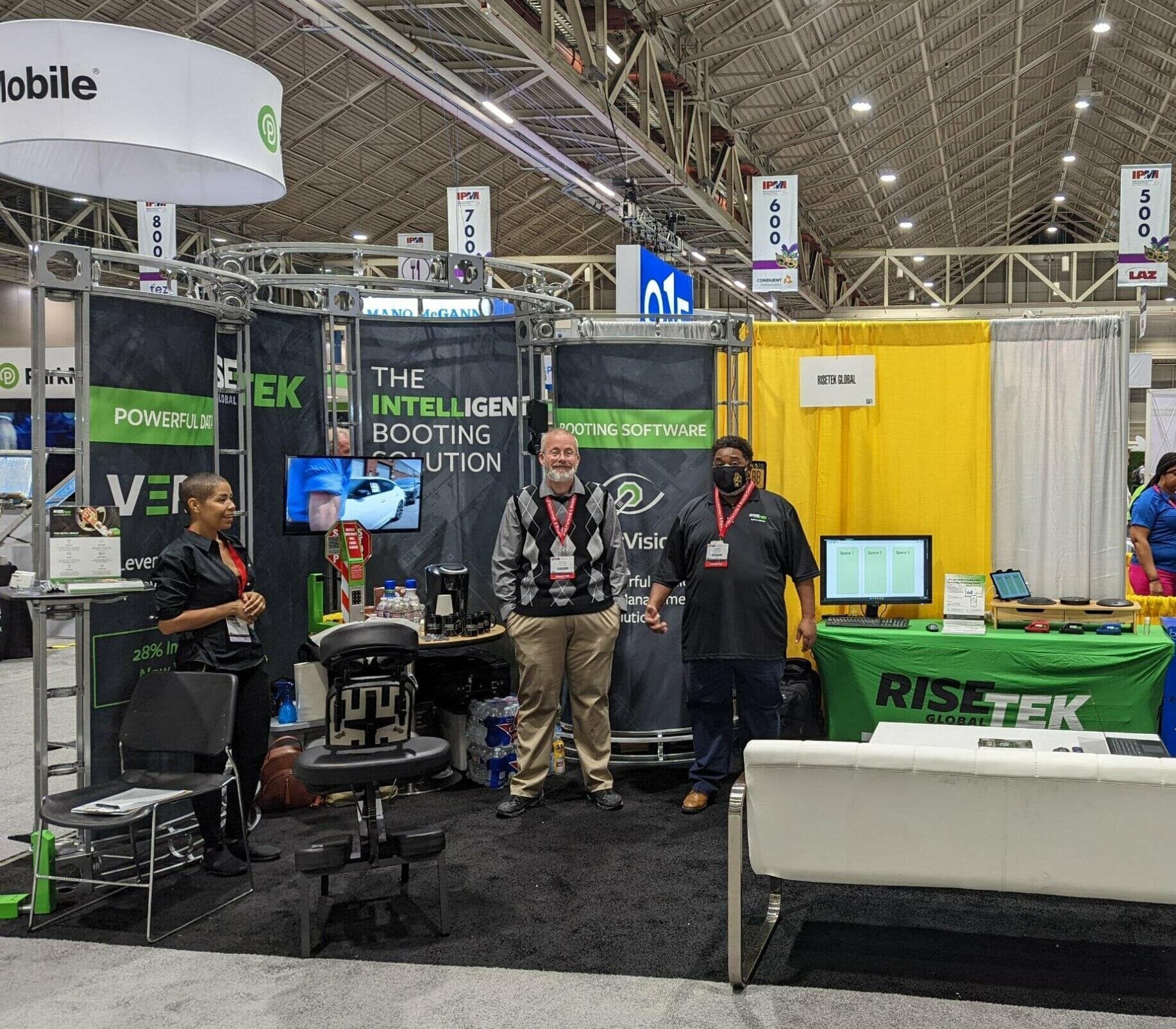 Three people stand at the RISETEK Global booth at the Apartmentalize Expo (NAA 2022), surrounded by tech displays. 